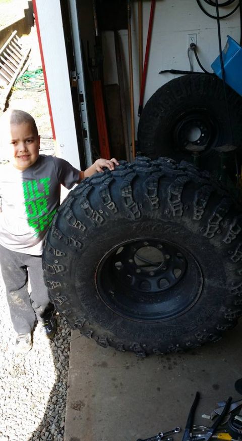 1984 Ford Bronco - A young boy poses next to a very large off-road tire, likely for a truck or SUV. The tire is black with aggressive tread and is resting on…