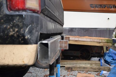 1984 Ford Bronco - A close-up, low-angle rear view of a custom metal trailer hitch being fabricated and attached to the frame of a dark-colored vehicle, possi…