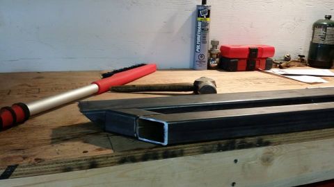 1984 Ford Bronco - A workbench is set up with various tools and materials, including a sledgehammer, a brush, a tube of polyurethane, and metal framing. Two r…