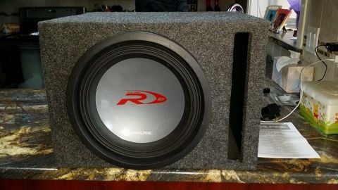 1984 Ford Bronco - A close-up, slightly angled view of an Alpine Type R 12-inch subwoofer in a gray carpeted enclosure. The subwoofer has a silver cone with a…