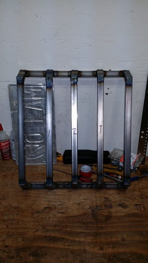 1984 Ford Bronco - A metal rack with numbered vertical bars is displayed on a wooden workbench. Behind the rack, a license plate and various tools and supplie…