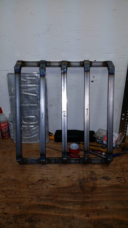 Metal rack with numbered bars on a workbench with tools and a license plate.
