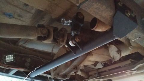 1984 Ford Bronco - The underside of a vehicle shows a modified suspension component, likely a track bar, installed between the frame and the rear axle. A driv…