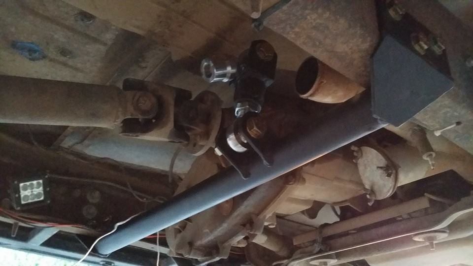 Underside of vehicle showing suspension modification, driveshaft, and exhaust.