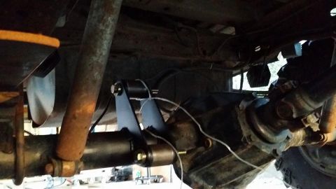 1984 Ford Bronco - Underneath view of a vehicle's rear axle and suspension components, showing a shock absorber, leaf springs, and a custom-looking bracket at…