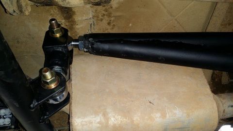 1984 Ford Bronco - A close-up view of the suspension linkage on a vehicle, showing black metal components, bolts, and a portion of the exhaust system.