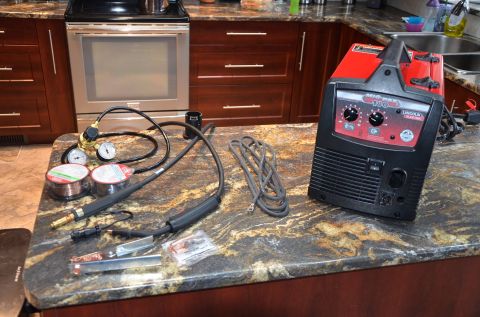 1984 Ford Bronco - A Lincoln Electric MIG Pak 180 welder and associated accessories are laid out on a granite countertop in a kitchen setting. The items inclu…