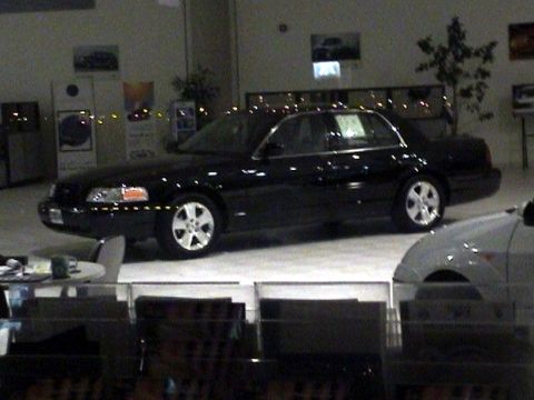 1999 Mercury Grand Marquis - A black sedan is parked in a showroom next to another vehicle.