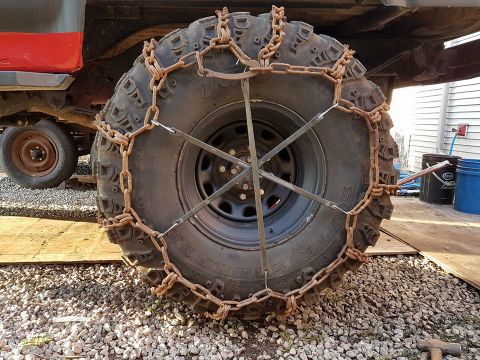 1984 Ford Bronco - A close-up view of a vehicle's tire fitted with snow chains, with a second tire visible behind it.