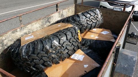 1984 Ford Bronco - Trailer loaded with new off-road tires. White SUV in background.