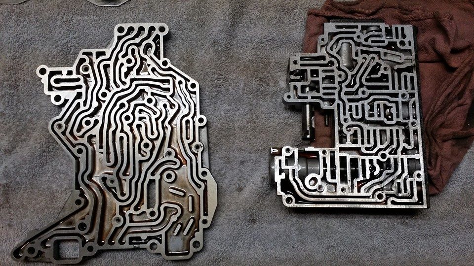 Two metal transmission valve bodies with complex channels on a gray surface