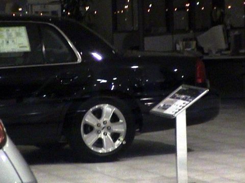 1999 Mercury Grand Marquis - A black sedan is parked indoors, possibly at a dealership, with a display stand next to it.