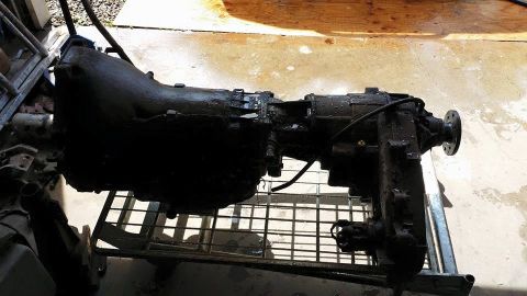1984 Ford Bronco - A greasy transmission and transfer case assembly is displayed on a metal rack, likely for repair or sale.