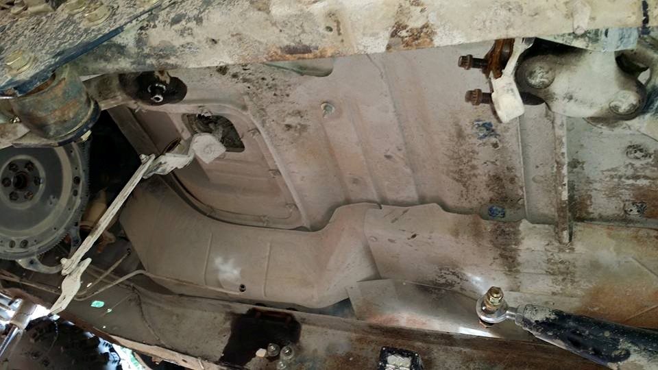 Underside view of a vehicle showing the transmission bell housing, exhaust pipe, and fuel tank