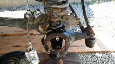 1984 Ford Bronco - Close-up of a vehicle's front axle suspension components, with a grease line connected to a Sprite can.