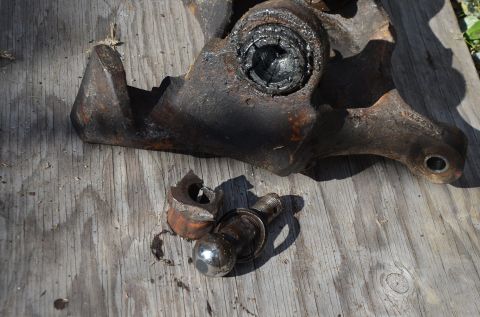 1984 Ford Bronco - Damaged ball joint and spindle assembly, likely from a vehicle, lies on weathered wood.