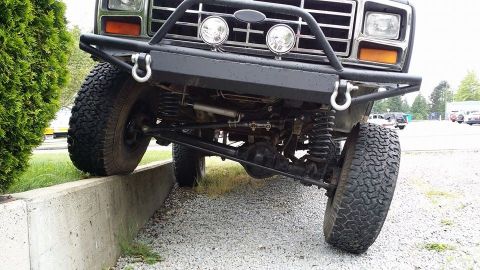 1984 Ford Bronco - The front suspension and bumper of a 1984 Ford Bronco are visible as it is driven onto a concrete curb.