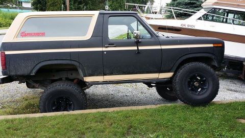 1984 Ford Bronco - Side view of a lifted black Ford Bronco with a tan stripe and removable top.