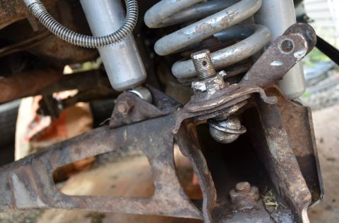 1984 Ford Bronco - Close-up view of a heavily corroded vehicle suspension system, showing a ball joint and shock absorber.