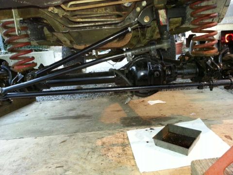 1984 Ford Bronco - Vehicle undercarriage with suspension and differential visible, along with a pan of used oil.