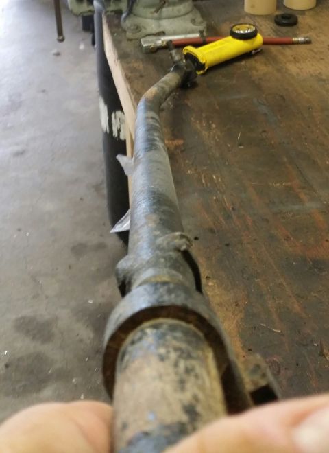 1984 Ford Bronco - A rusty exhaust pipe lies on a wooden workbench next to a yellow tool.