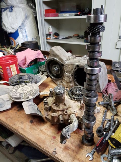 1984 Ford Bronco - Engine components including a camshaft, water pump, and transmission case are disassembled on a workbench.