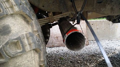 1984 Ford Bronco - A close-up view of a vehicle's undercarriage reveals a large tire and a custom exhaust pipe.