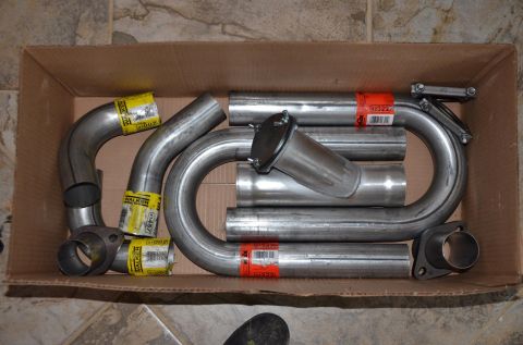 1984 Ford Bronco - A collection of exhaust pipe components are neatly arranged inside a cardboard box, ready for installation.