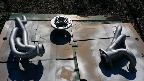 1984 Ford Bronco - Two exhaust manifolds and a hub are laid out on a surface, possibly for painting or repair.