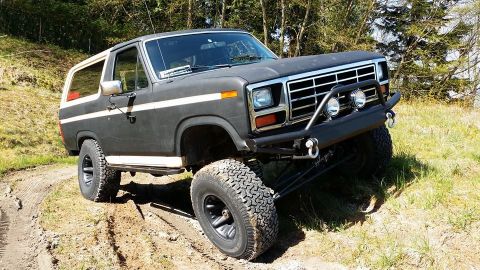 1984 Ford Bronco - This lifted Ford Bronco is navigating a dirt trail with trees in the background.