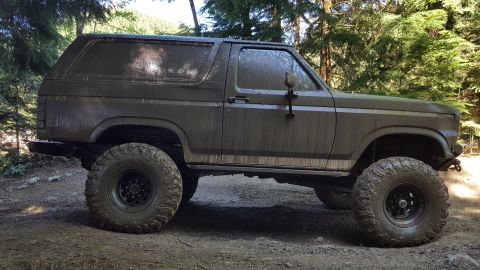 1984 Ford Bronco - This SUV, likely from the early 1980s, is heavily covered in mud, suggesting off-road use.