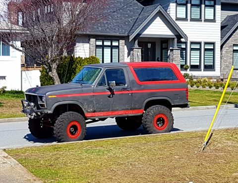 1984 Ford Bronco - This modified Ford Bronco is parked on a residential street with modern houses in the background.