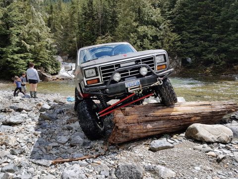 1984 Ford Bronco - Modified Ford Bronco navigating rough terrain near a river.