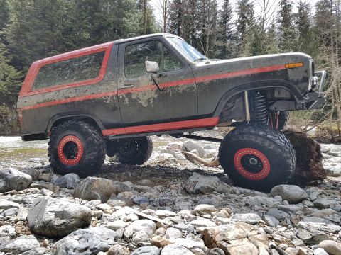 1984 Ford Bronco - Modified 1980s Ford Bronco with large off-road tires navigates a rocky riverbed.