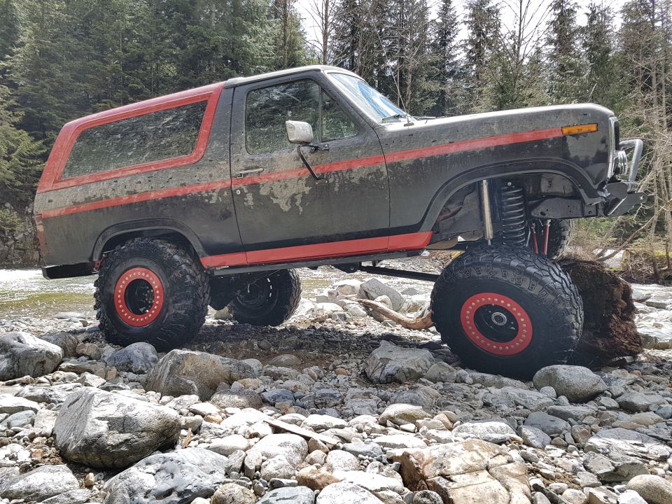 Lifted 1980s Ford Bronco with red stripes on rocky terrain