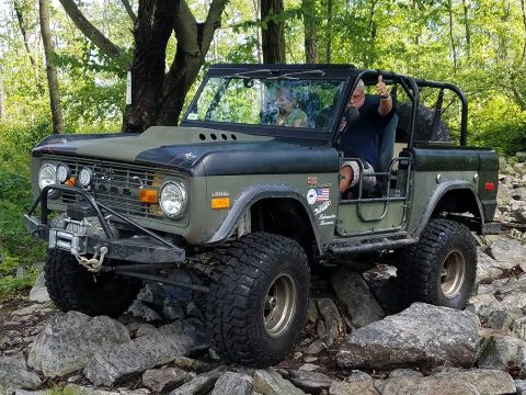 1972 Ford Bronco - Modified 1972 Ford Bronco tackling a challenging off-road course with a driver giving a thumbs up.