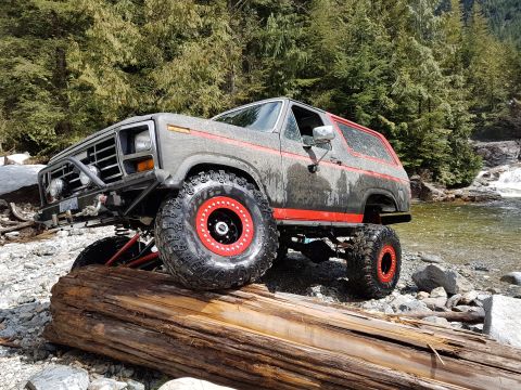 1984 Ford Bronco - This heavily modified Ford Bronco is positioned on a fallen log next to a flowing river and rocky terrain.