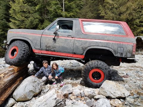 1984 Ford Bronco - This lifted 1980 Ford Bronco, modified for off-roading, is shown with two children posing in the rocky terrain.