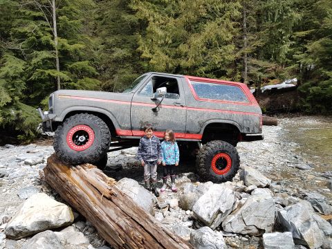 1984 Ford Bronco - A heavily modified Ford Bronco is shown off-road with two children posing beside it.