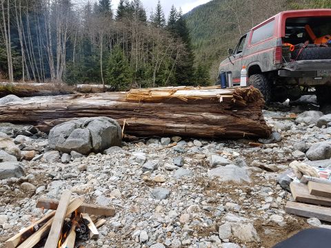 1984 Ford Bronco - A red and black Ford Bronco is parked on a rocky riverbed next to a large fallen log. The vehicle's rear is visible, loaded with gear, and…