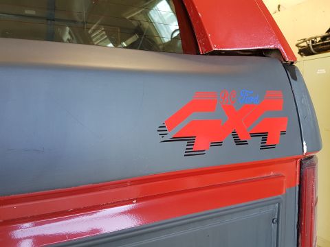 1984 Ford Bronco - The rear passenger side of a gray Ford Bronco with a red stripe and a red "4x4 BC Ford" decal. The vehicle is parked indoors, possibly in a…