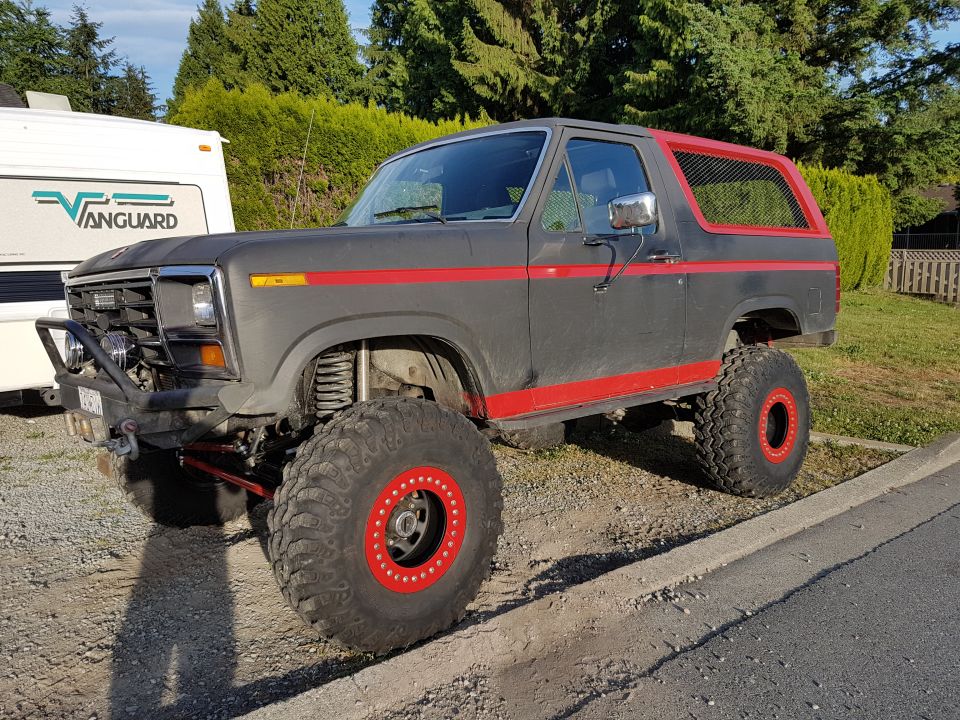 Lifted dark gray Ford Bronco with red trim and large off-road tires.