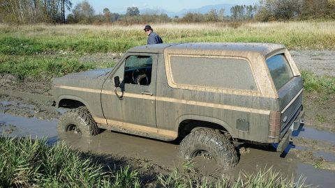 1984 Ford Bronco - Muddy Ford Bronco stuck in a field, with a person standing on the roof.