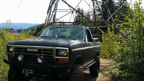 1984 Ford Bronco - This modified Ford Bronco is parked on a dirt road next to a tall industrial tower.