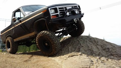 1984 Ford Bronco - A black Ford Bronco navigates a rocky incline, its lifted suspension and off-road capabilities.