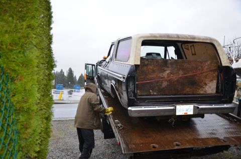 1984 Ford Bronco - A person loads a Ford Bronco onto a tow truck. The rear cargo area is covered with plywood.
