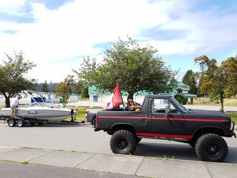 1984 Ford Bronco - A lifted pickup truck tows a boat on a trailer, with a Canadian flag displayed in the truck bed.