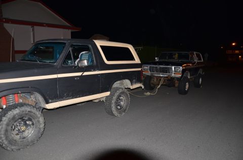 1984 Ford Bronco - A Ford Bronco is towing another Ford Bronco at night. The front vehicle's grille suggests a 1978 model year.