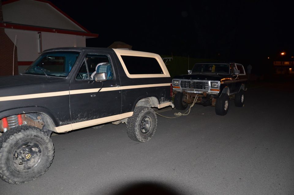 Two Ford Broncos, one towing the other. The front Bronco appears to be from the late 1970s