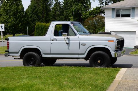 1984 Ford Bronco - Side view of a light gray Ford Bronco with a black roof and black wheels.